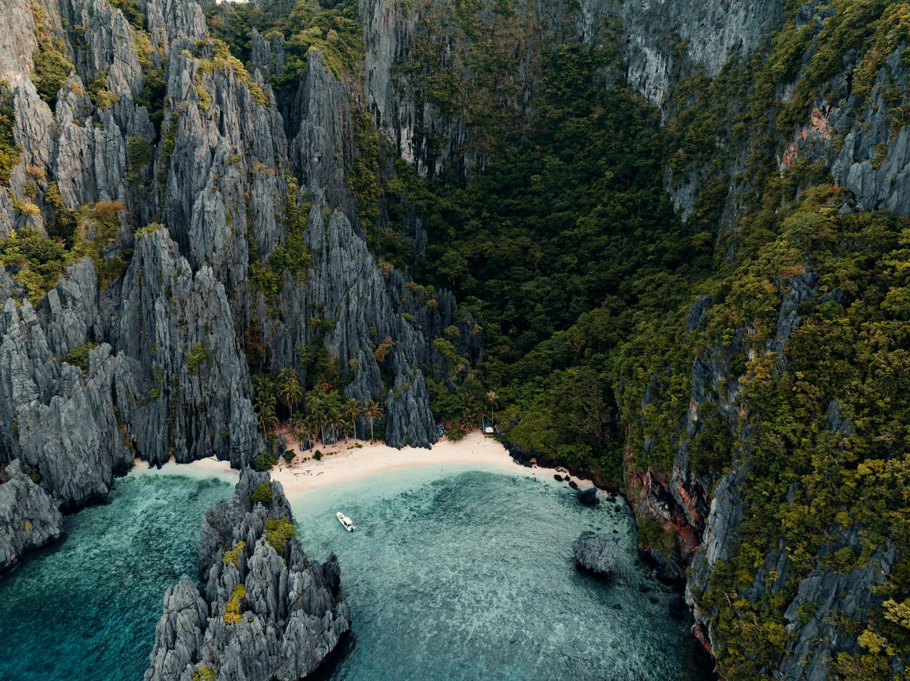 A white sand cove beneath monumental limestone cliffs in El Nido, Palawan